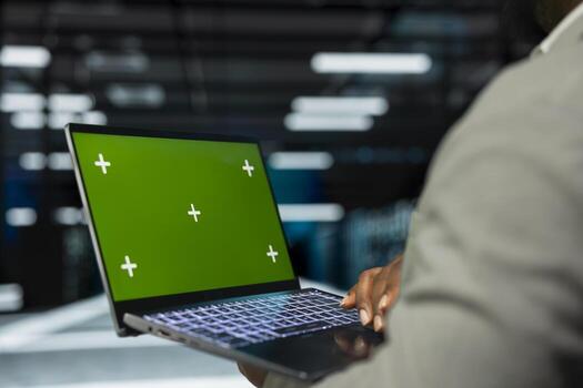 Close up of engineer in data center using isolated screen laptop to check for server performance issues. IT professional in server hub fixing errors slowing down hardware using mockup notebook photo