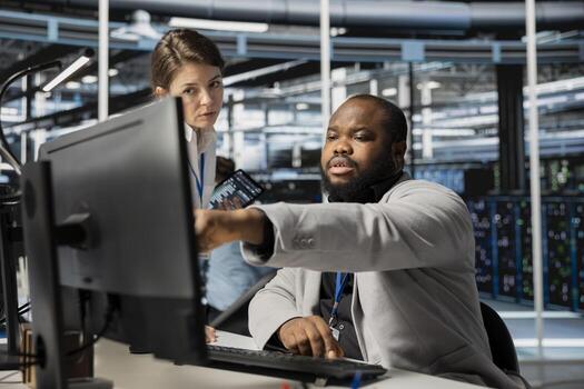 Data center manager supervising engineer running diagnostic scripts on computer, examining gear. Server room supervisor overseeing worker using PC to evaluate rackmounts performance metrics photo