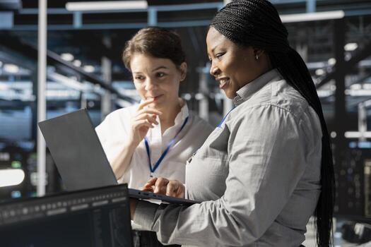 Smiling engineering team using laptop in data center, managing server virtualization, running scripts. Happy coworkers using programming language on notebook in server farm photo