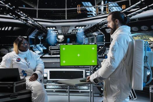 Researchers travelling in space with starship conducting scientific experiments in orbit using green screen monitor. Scientists using mockup display to document experimental observations photo