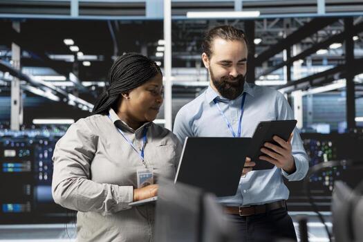 Happy system administrators in data center using devices, verifying firewall configurations. Jolly teamworking IT experts performing equipment vulnerability scans in server hub photo