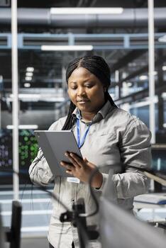 Woman in data center doing software updates, verifying deep learning parameters. African american server hub IT expert using PC to inspect configurations, ensuring optimal application performance photo