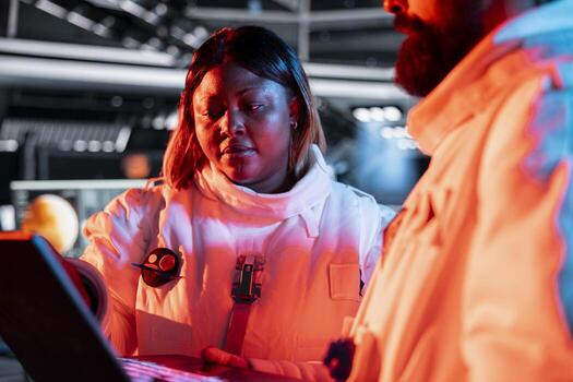 Orbit station technicians troubleshooting red warning light flashing issue. Team of spaceship engineers using notebook to fix damaged hardware electronics affecting operations photo