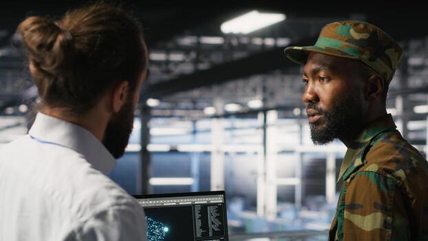 Military server room IT professionals using AI LLM tech on laptop to review network performance. Army operators manage hardware systems supporting mission critical connectivity photo