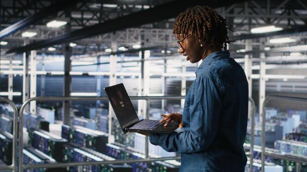 Data center software developer panicking after receiving critical error popup on laptop display. African american woman in server hub alerted by bugs causing low hardware performance photo