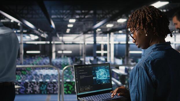 System administrators in data center monitoring AI LLM visualization. African american server farm coworkers overseeing rigs powering machine learning processes, photo