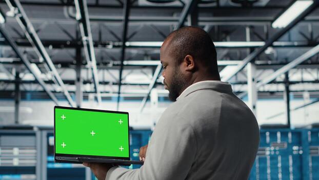 Data center admin using isolated screen laptop to monitor neural network AI. Server room employee using mockup notebook to oversee rigs powering machine learning processes, camera B photo