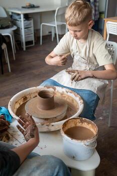 Child and instructor shaping clay together at pottery workshop photo
