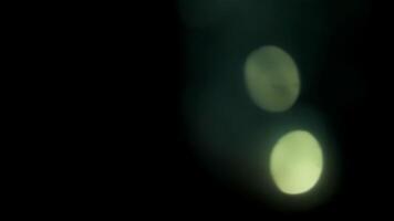 suave verde bokeh orbes cintilar e deriva para a direita através uma Sombrio fundo, criando a abstrato, brilhando e cinematográfico luz efeito dentro suave movimento. video