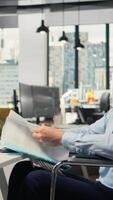 Vertical Portfolio manager in wheelchair looks over documentation files to evaluate capital allocation. Prop firm expert with disability reading paperwork documents, researching, camera A video