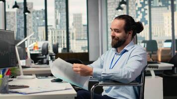 portfölj chef i rullstol utseende över dokumentation filer till utvärdera huvudstad tilldelning. stötta fast expert- med handikapp läsning pappersarbete dokument, forska, kamera b video