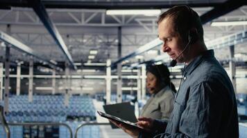 Data center admin talking in audio headset mic, helping clients resolve website hosting problems. Server farm worker on industrial platform helping users keep online services running, camera A video