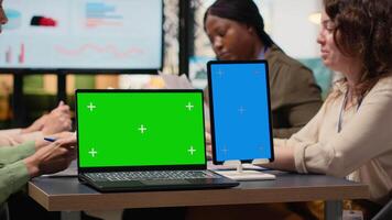affärskvinna arbetssätt sida förbi sida med en grön skärm på de tabell, samarbetande på en strategisk presentation den där skulle kunna funktion projiceras rapporter, analys, eller Framgång metrik. kamera b. video