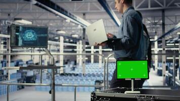 Close up of green screen tablet in front of data center engineers improving AI rigs. Server hub colleagues manage gear using mockup device to support artificial intelligence workloads, camera A video
