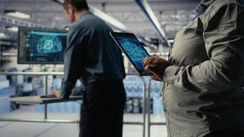 Close up of data center system administrators deploying deep learning software on rigs. Team of server hub IT experts train AI systems with datasets using tablet to support applications, camera A video