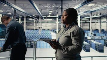 Software developers monitor server hub activity using tablet. Data center employees doing brainstorming, reviewing equipment tests results on devices to ensure systems are working correctly, camera A video