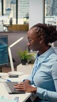 vertical comerciante dentro escritório alavancagens ai tecnologia em pc para interpretar analytics gráficos, otimizando comprando e vendendo. africano americano mulher usa profundo Aprendendo automatização para maximizar lucros, Câmera uma video