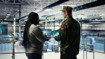 Army commander and software developer in data center integrating AI into radar systems for missile tracking. Soldier and female programmer in server hub analyzing aerial movement on laptop, camera A video