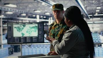 squadra di militare specialisti nel dati centro guardare a mondo carta geografica su schermo, coordinamento missione zone. esercito colleghi nel server centro guardare a globale carta geografica per Piano campo di battaglia operazioni, telecamera B video