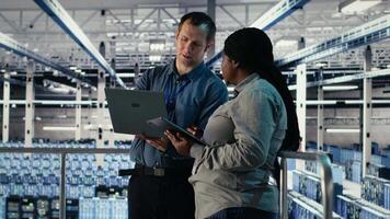 Server room coworkers scan infrastructure for security issues using laptop. Data center system administrators using notebook to organize file backups and plan recovery steps, camera B video