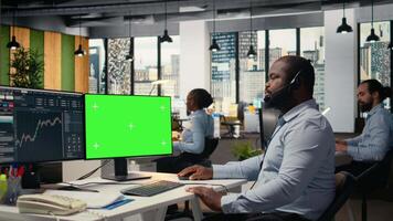 financiero tutor utilizando verde pantalla computadora ofertas inversión Guia durante cliente llamadas africano americano hombre hablando en auriculares micrófono, Ayudar clientes construir portafolio utilizando Bosquejo ordenador personal, cámara un video