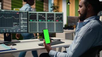 Equity analyst using green screen smartphone to reviews quarterly earnings, assessing stock market value. Trader conducts financial analysis using mockup mobile phone to improve investments, camera A video