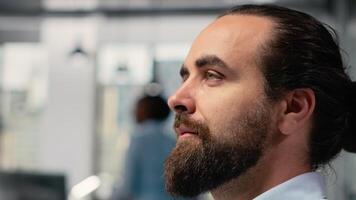 Trader in office looking upward with subtle smile on face, visualizing financial independence and future success. Optimistic stockbroker at PC desk dreaming of wealth and economic freedom, camera B video