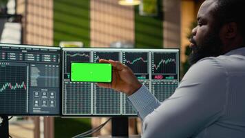 fondkommissionär använder sig av attrapp smartphone till Kolla på handel pedagogisk innehåll. tillgång förvaltning företag anställd i kontor lär ny handel strategier från lektion på isolerat skärm telefon video
