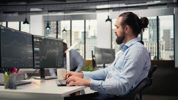 Close up of happy trader in prop firm workplace analyzing market data and executing trades using trading software interface on PC. Joyous stockbroker at work monitoring stock prices, camera A video