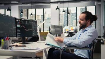 portfölj chef i rullstol utseende över dokumentation filer till utvärdera huvudstad tilldelning. stötta fast expert- med handikapp läsning pappersarbete dokument, forska, kamera en video