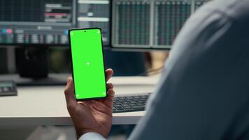 Equity analyst using green screen smartphone to reviews quarterly earnings, assessing stock market value. Trader conducts financial analysis using mockup mobile phone to improve investments, camera B video