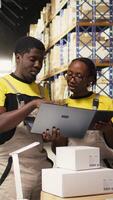 vertikal svart team medlemmar hantering paket data på bärbar dator för beställa bearbetning i logistik nav, verifierande pallar frakt etiketter för distribution protokoll. effektiv e-handel lager. kamera a. video