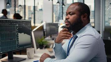 cerca arriba de comerciante analizando valores intercambiar analítica, haciendo pensamiento, evaluando comercio estrategia en apuntalar firma oficina. africano americano hombre lluvia de ideas, evalúa riesgo en financiero mercados, cámara un video