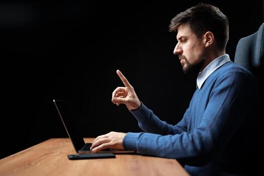 hombre trabajando atentamente en un ordenador portátil mientras gesticulando en un oscuro oficina ambiente durante noche horas foto
