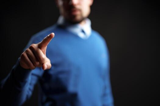 Man in blue sweater points forward, indicating importance in a minimalist setting photo