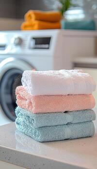 Neatly folded colorful towels stacked on a kitchen counter with laundry machine in the background photo