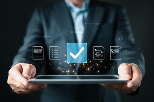 A business professional holds a tablet displaying floating document icons, a large checkmark symbolizing digital approve processes, focusing on business quality assurance and data management. photo