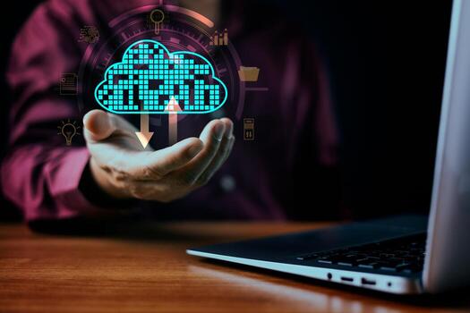 A businessman setting interacts with a glowing digital cloud icon featuring download arrows, symbolizing cloud computing, data security, and network infrastructure. A laptop sits on the wooden desk. photo