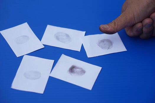 Close-up of fingerprint identification process. A person inked thumb is used to print on white paper cards, symbolizing personal identification, forensic evidence, and biometric security systems. photo