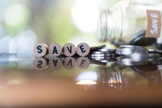apilado monedas en vaso tarro con salvar escrito en un de madera bloquear y más monedas en el mesa. foto