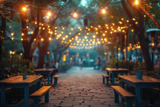 A cobblestone pathway lined with wooden tables and benches under a canopy of trees illuminated by warm string lights. photo