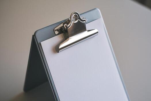 A close-up of a clipboard with a blank notepad resting on a light surface. photo