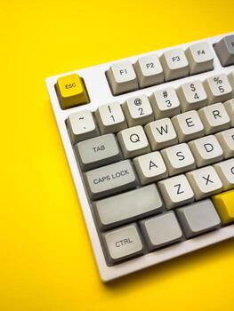 White mechanical keyboard with bright Esc key on bright yellow background, minimalism photo
