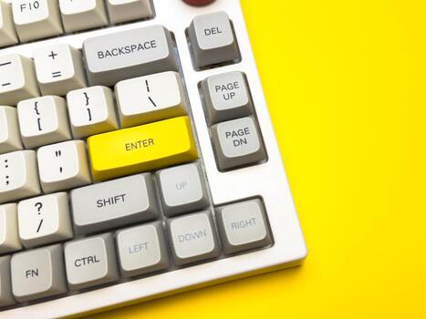 White keyboard with bright Enter key on bright yellow background, minimalism, keyboard buttons. A keyboard with a yellow key on the bottom left photo
