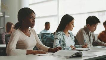 diverso studenti messa a fuoco su loro studi nel un' luminosa, moderno Università aula. essi collaborare su Compiti mentre seduto a tavoli, promuovere un' supporto educativo ambiente. video