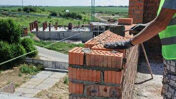 albañil colocación final fila en alto pared. construcción trabajador en guantes y la seguridad chaleco alinea hueco ladrillos con un cuerda guía mientras refinamiento el parte superior fila de video