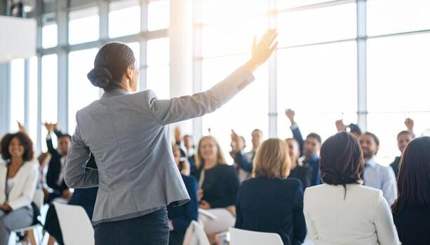 Professional speaker engages audience in bright conference hall, with attendees raising their hands to participate. atmosphere is dynamic and interactive, showcasing vibrant business environment photo