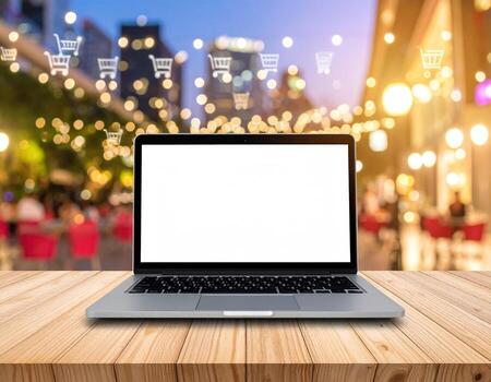 Laptop on wooden table with shopping cart and lights in background photo