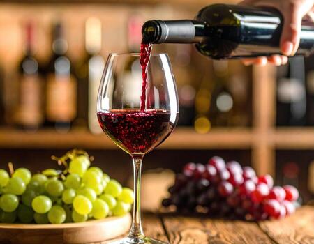 Ruby red stream of wine is poured into crystal glass, surrounded by fresh green and purple grapes, creating warm and inviting atmosphere perfect for wine lovers photo