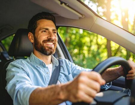 Man is driving car and smiling, surrounded by lush green trees and peaceful atmosphere, enjoying moment with high fidelity photo